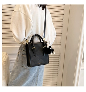 Detailed view of black quilted crossbody bag with gold hardware and plush pom-pom charm