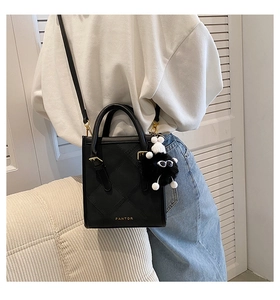 Detail of black quilted leather crossbody bag with golden hardware and plush pendant