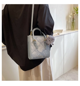 Detail of light blue denim texture shoulder bag with plush charm on a female model