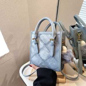 Light blue denim texture mini tote bag with gold hardware and plush charm shown in a mirror