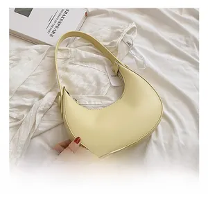 Top view of a minimalist light yellow crescent shoulder bag on white fabric background