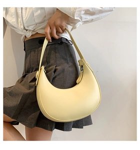 Close-up of minimalist cream yellow crescent shoulder bag worn by model in soft light
