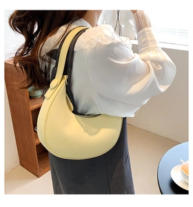 Detail of light yellow leather hobo bag worn by a model in a minimalist interior setting