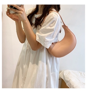 Detail of the pale pink crescent underarm bag worn with a white dress on a model