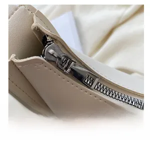 Close-up of smooth metal zipper detail on cream minimalist crossbody shoulder bag