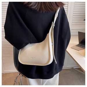 Close-up of beige crescent shoulder bag with wide strap on model in office setting