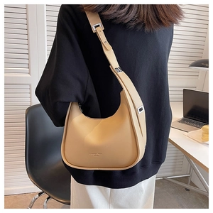 Modern beige crescent shoulder bag made of smooth leather with adjustable strap shown in use