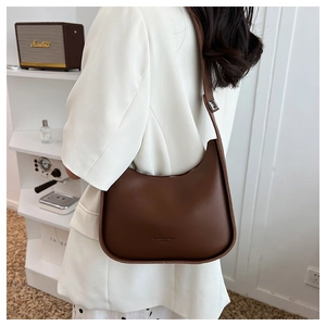 Detail of dark brown faux leather crescent bag with adjustable strap worn by model