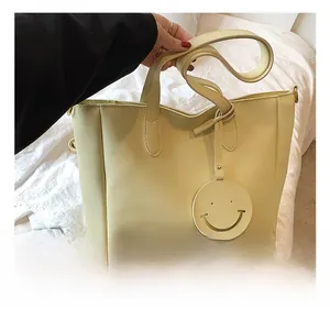 Detail of creamy yellow tote bag with long shoulder strap and a cute smiley pendant