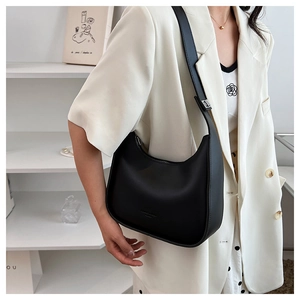 Close-up of black matte hobo bag with adjustable strap worn by model in white suit
