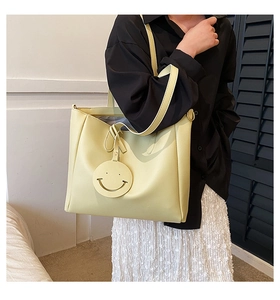 Detail of yellow tote bag featuring a cute smiley face pendant and wide shoulder straps