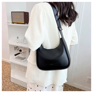 Minimalist black crescent shoulder bag shown on model in a stylish interior setting