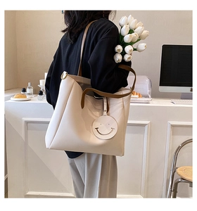 Off-white large tote bag with brown straps and smiley charm in a lifestyle setting