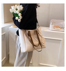 Detail view of large cream tote bag with brown leather straps and cute smiley charm