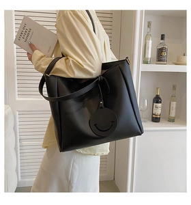 Close-up of large black leather tote bag with a unique round smiley face charm detail