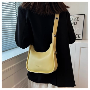 Detailed view of a light yellow crescent saddle bag worn over a black blazer
