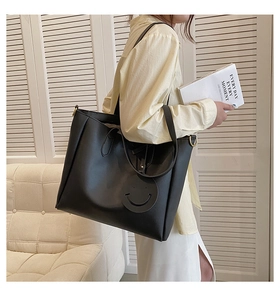 Close-up of a black tote bag with a smiley charm on a model in a cozy indoor setting