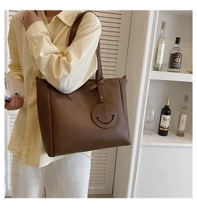 Detail of dark brown faux leather tote bag with a minimalist smiley face leather pendant