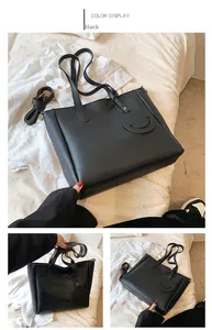 Detail of black large capacity tote bag with long strap and smiley face pendant