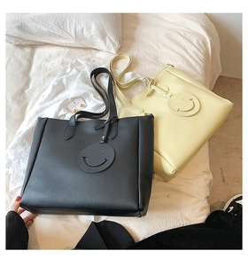 Detail view of large tote bags in black and cream featuring a signature smiley face tag