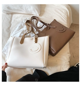 Detail of minimalist cream and brown tote bags with a round smiley face charm accessory