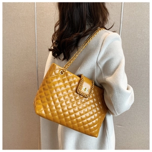 Detail of yellow quilted tote bag with golden chain strap and metallic square lock closure