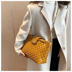 Detail of a mustard yellow quilted tote bag with golden chain strap and metal lock closure