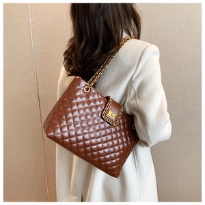 Detail of glossy quilted pattern on brown tote bag with golden metal chain strap