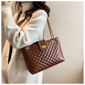 Detail of dark brown quilted tote bag with gold chain strap worn by a model