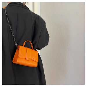 Detail of orange faux crocodile texture bag with black chain strap on black blazer