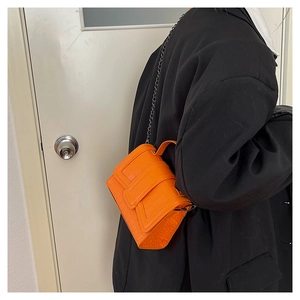 Detail view of bright orange stone-patterned handbag with metal chain on a model