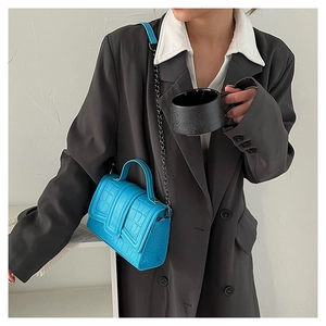 Detail of bright blue faux crocodile leather bag with metal chain strap and top handle