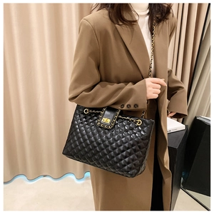 Detail of black quilted tote bag with gold hardware and leather chain strap worn by a model