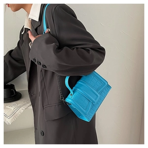 Detail of bright blue faux-crocodile leather bag with chain strap worn with a grey blazer