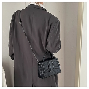 Macro detail of black crocodile embossed leather texture on a stylish crossbody handbag