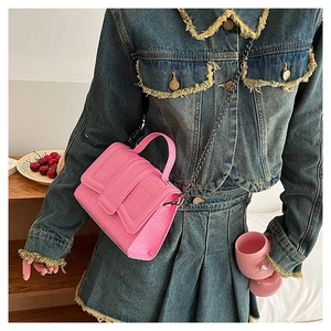 Detail of pink faux leather crossbody bag featuring crocodile texture and metal chain strap