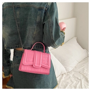 Detail of bright pink croc-embossed handbag with metal chain strap worn on denim outfit