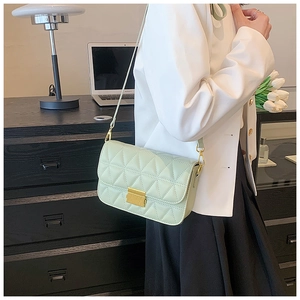 Detailed view of light green quilted crossbody bag with gold lock and chain strap on a model