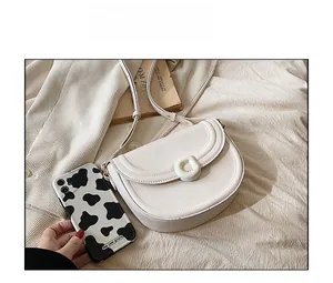 White minimalist saddle bag shown next to a smartphone for size reference and scale
