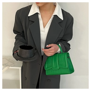 Close-up of green crocodile texture handbag paired with a grey blazer for a modern look