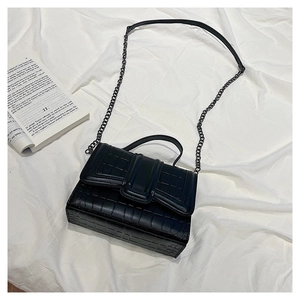 Detailed macro view of black crocodile pattern faux leather and metal chain on a handbag