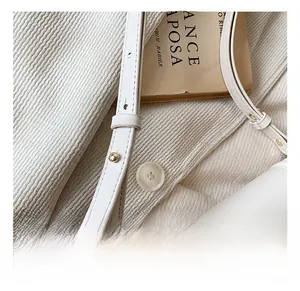Close-up of off-white leather shoulder strap featuring adjustable golden metal rivets
