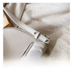 Detail showing golden hardware buckle, rivets, and precision stitching on white saddle bag