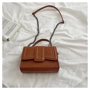 Detail of caramel brown faux leather handbag with crocodile pattern and metal chain strap