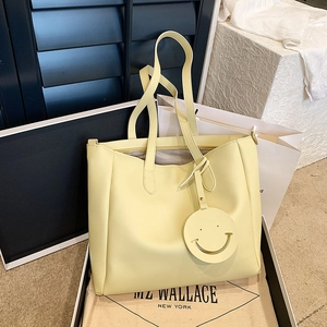 Light yellow leather tote bag with smile charm and long strap in premium packaging