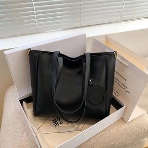 Black leather tote bag with smiley charm in a white gift box for stylish commuting
