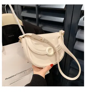 Detail of cream patent leather saddle bag with resin buckle and adjustable strap