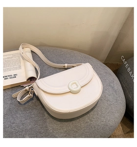 Detail of a cream faux leather saddle bag with D-ring buckle on a soft grey stool