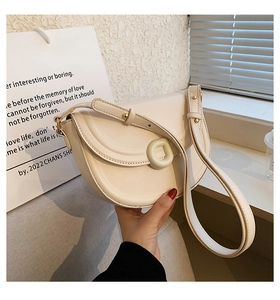 Close-up of cream faux leather saddle bag with circular buckle and adjustable strap