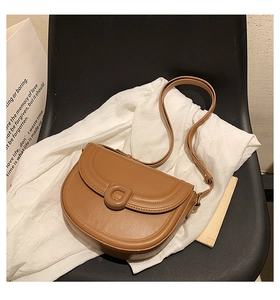Detail of a brown leather saddle bag featuring a classic rounded flap and round buckle